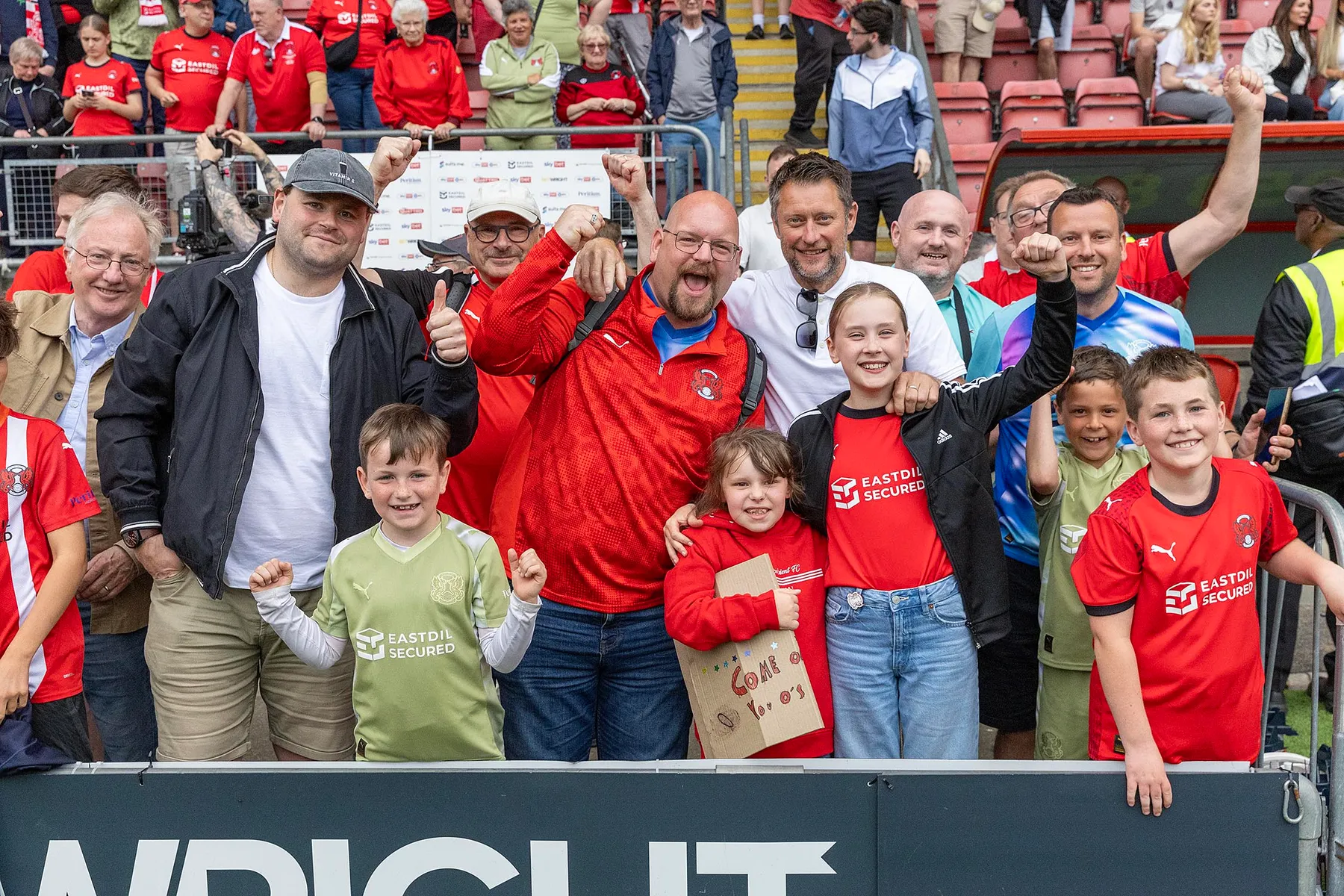 Leyton Orient supporters of different ages smiling together at the front of the stand