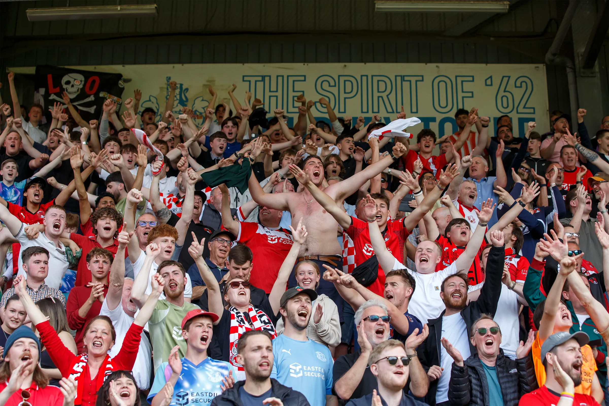 Leyton Orient supporters celebrating together beneath The Spirit of '62 sign