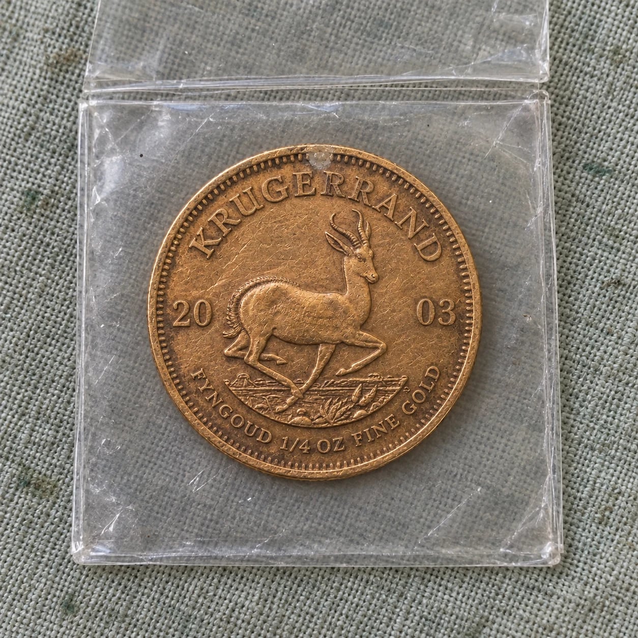 A complete worn 2003 quarter-ounce Gold Krugerrand coin in a plastic flip
