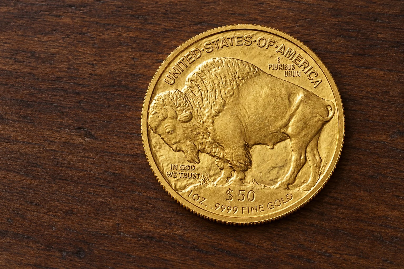 A complete handled one-ounce American Gold Buffalo coin showing the bison reverse on a clean walnut table