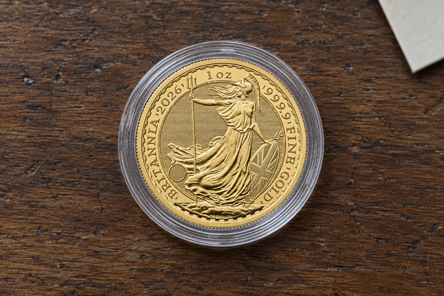 A one-ounce Gold Britannia coin in a clear capsule on a wooden table