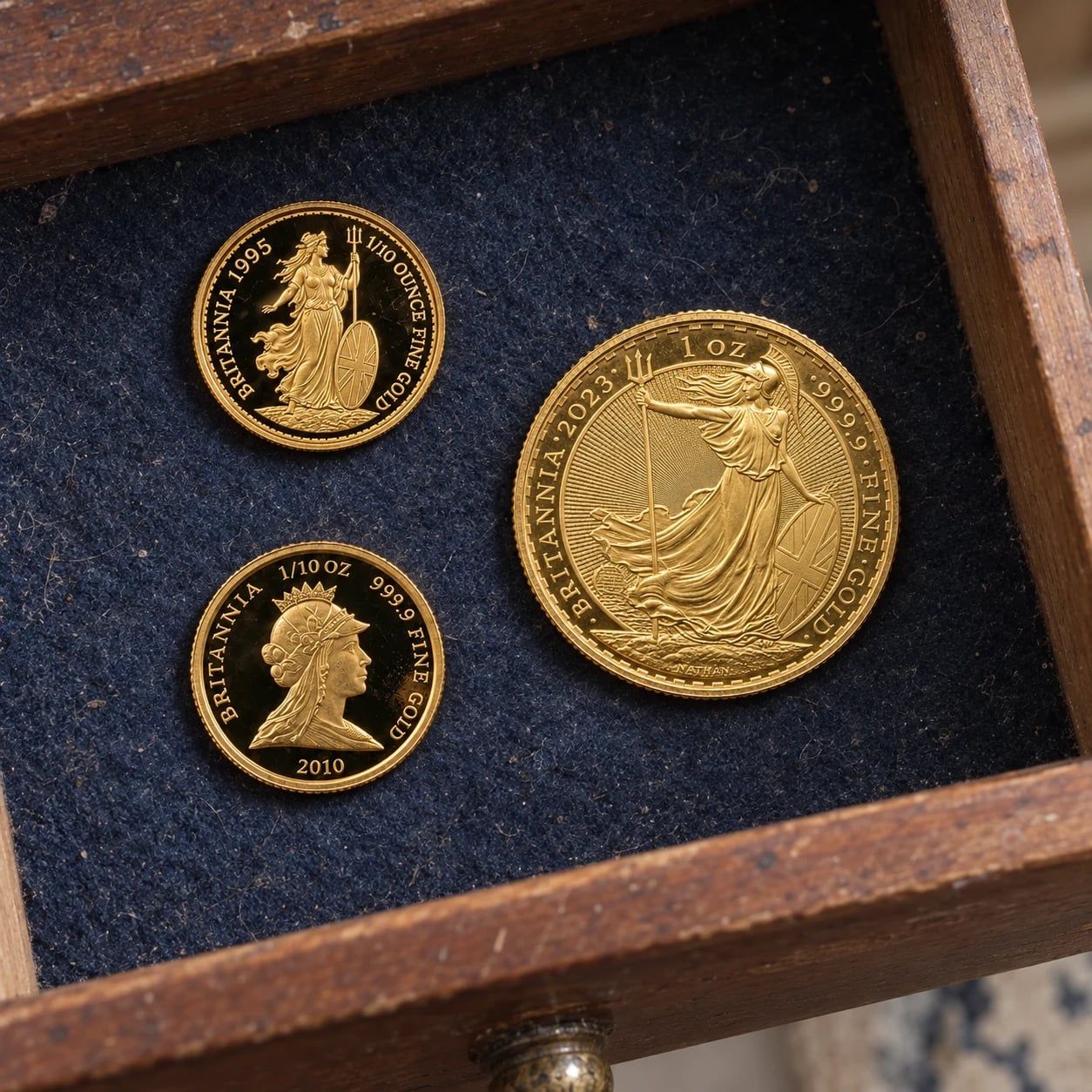 Three complete Gold Britannia coins from 1995, 2010 and 2023 stored in a wooden drawer