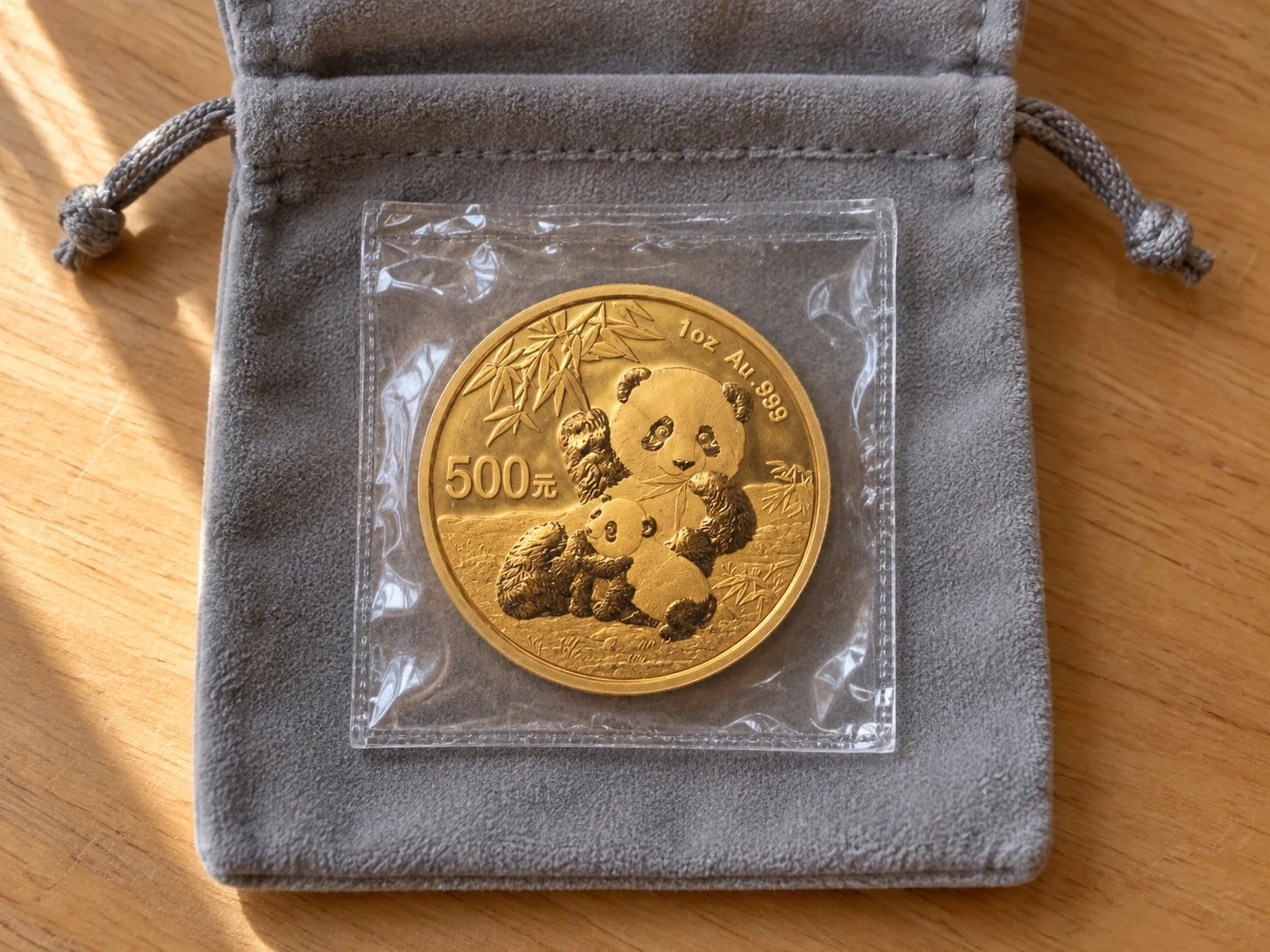 A complete older one-ounce Chinese Gold Panda coin in a clear mint-style sleeve and grey keepsake pouch