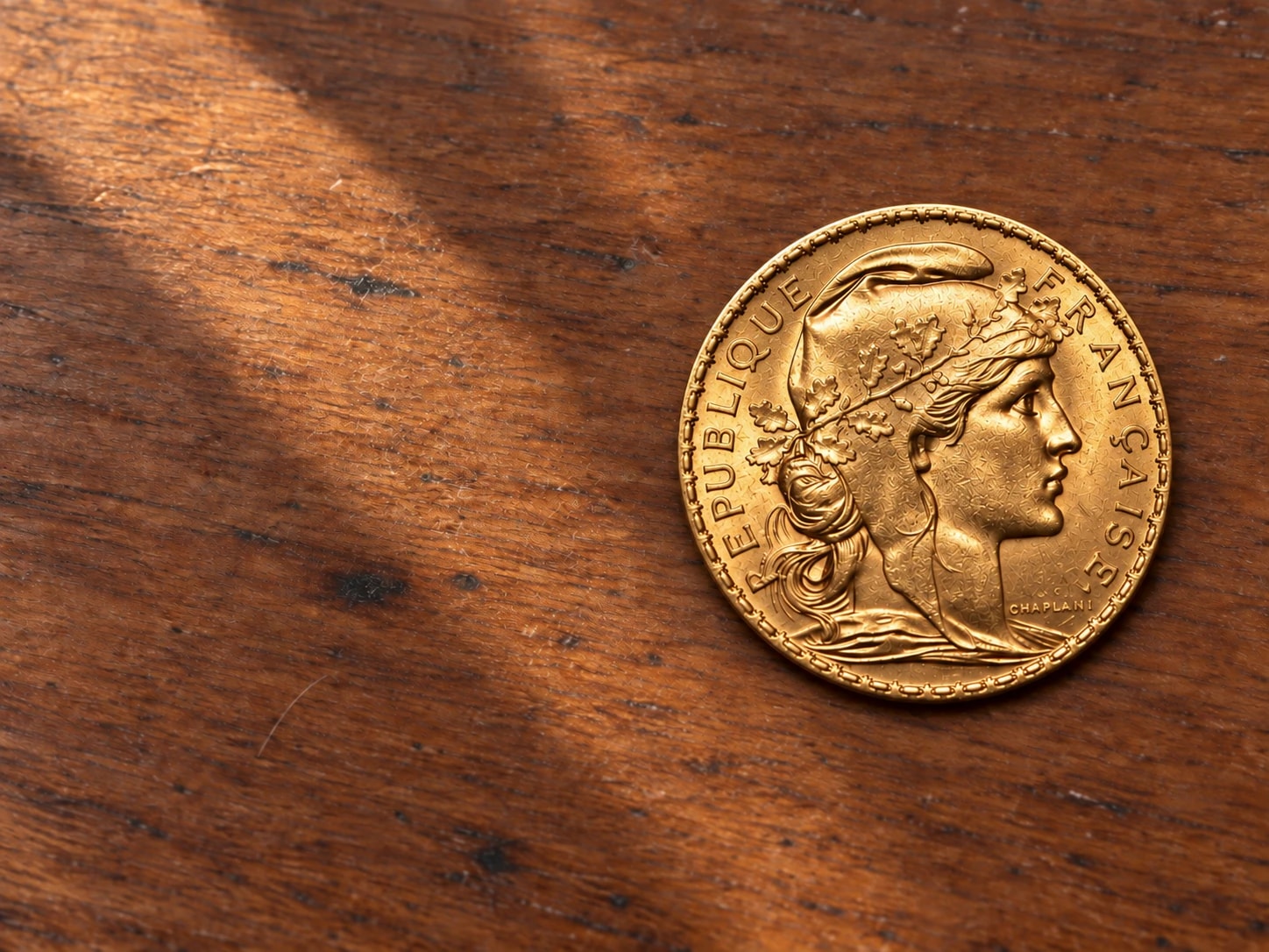 A complete 1908 French 20 Franc Marianne gold coin on a walnut table