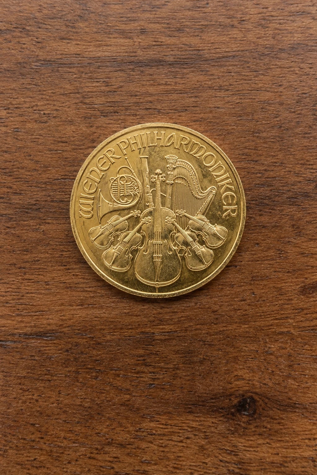A complete one-ounce Austrian Gold Philharmonic coin lying flat on a clean walnut table