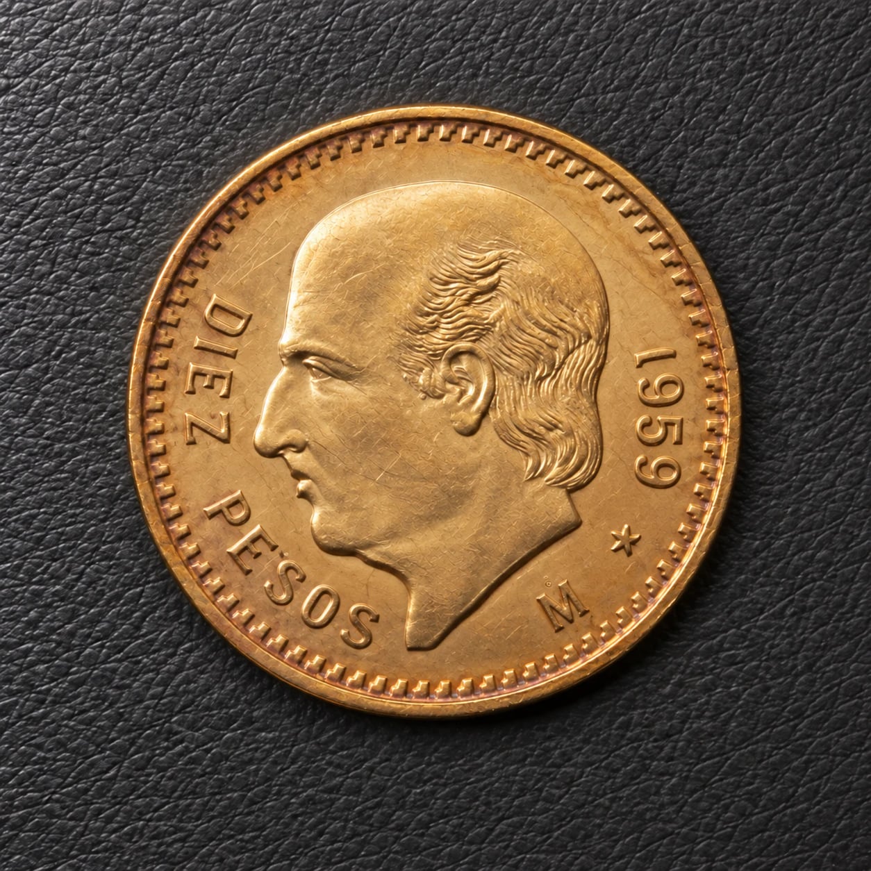 A complete 1959 Mexican 10 Pesos Hidalgo gold coin with rim toning on charcoal leather
