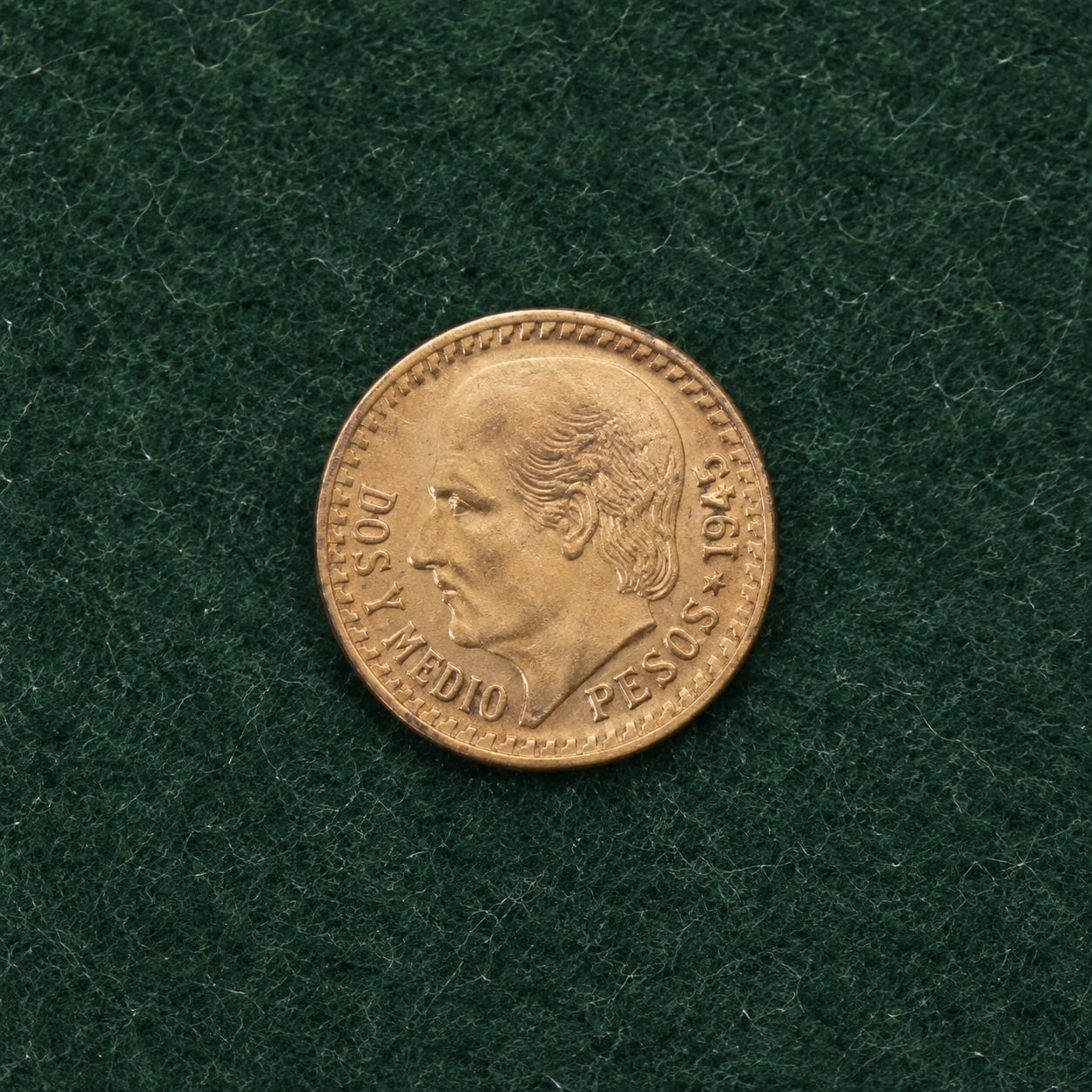A complete 1945 Mexican 2.5 Pesos Hidalgo gold coin with mild toning on green wool