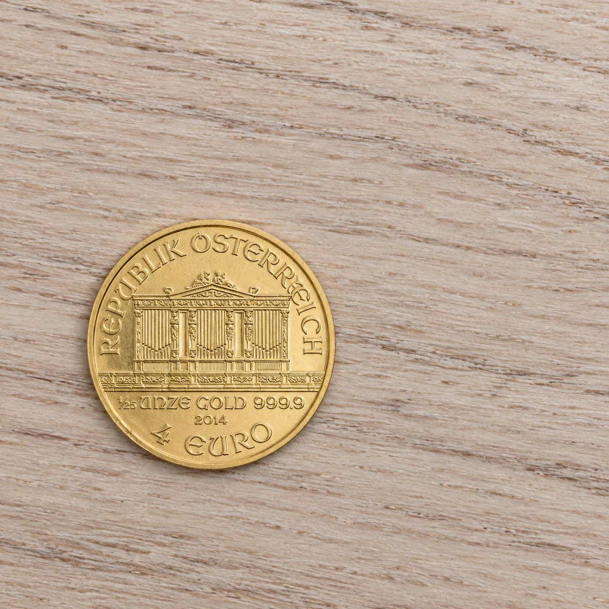 A complete lightly marked 2014 one-twenty-fifth-ounce Austrian Gold Philharmonic coin on a pale ash table