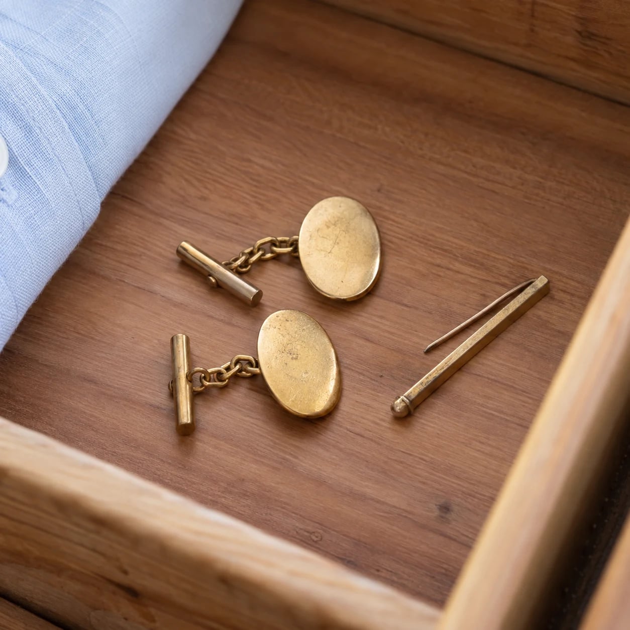 A pair of worn gold cufflinks and a slim tie pin in a shirt drawer