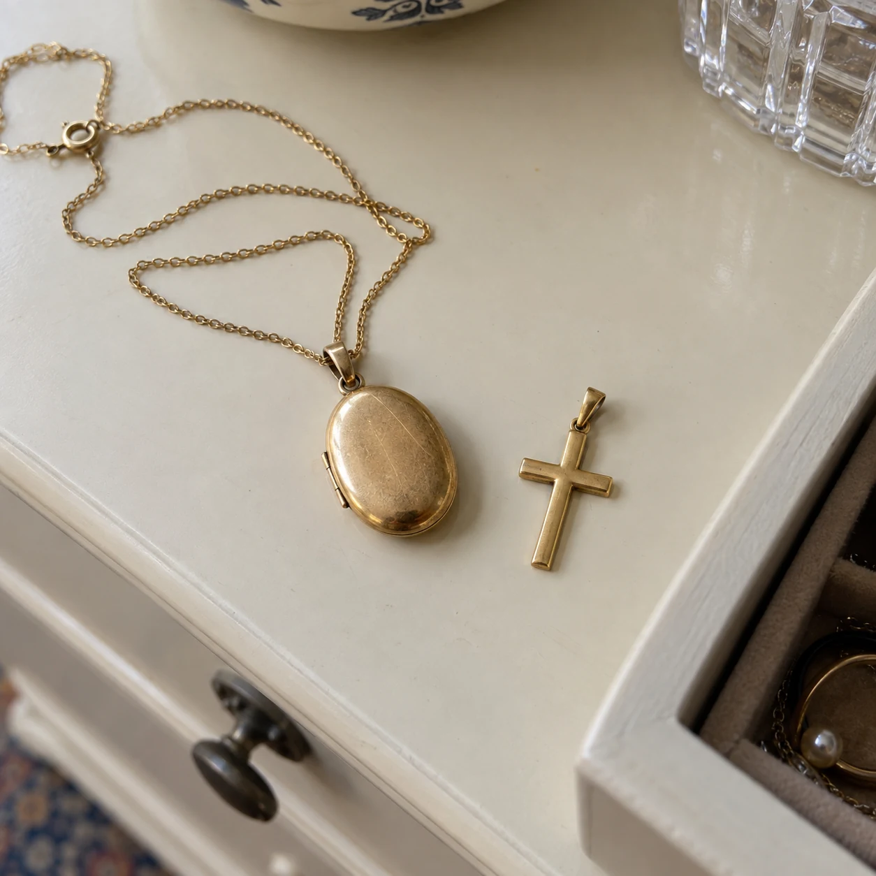 A worn gold locket on a chain beside a small gold cross pendant