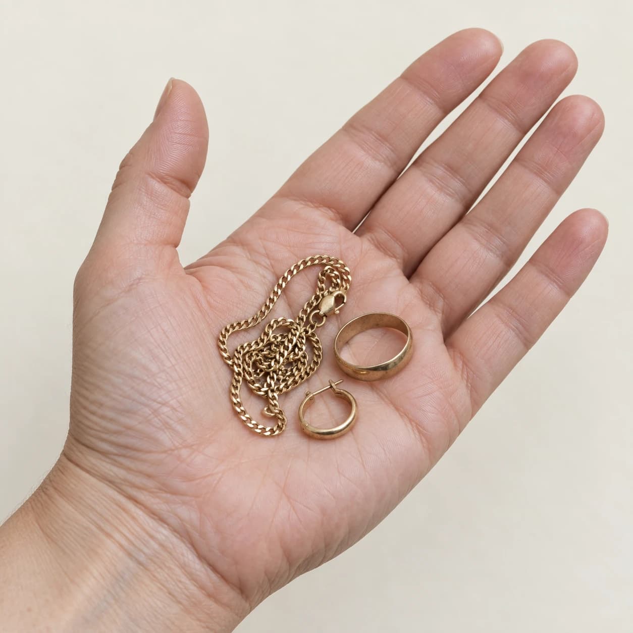 An open hand holding a worn gold chain, wedding ring and hoop earring