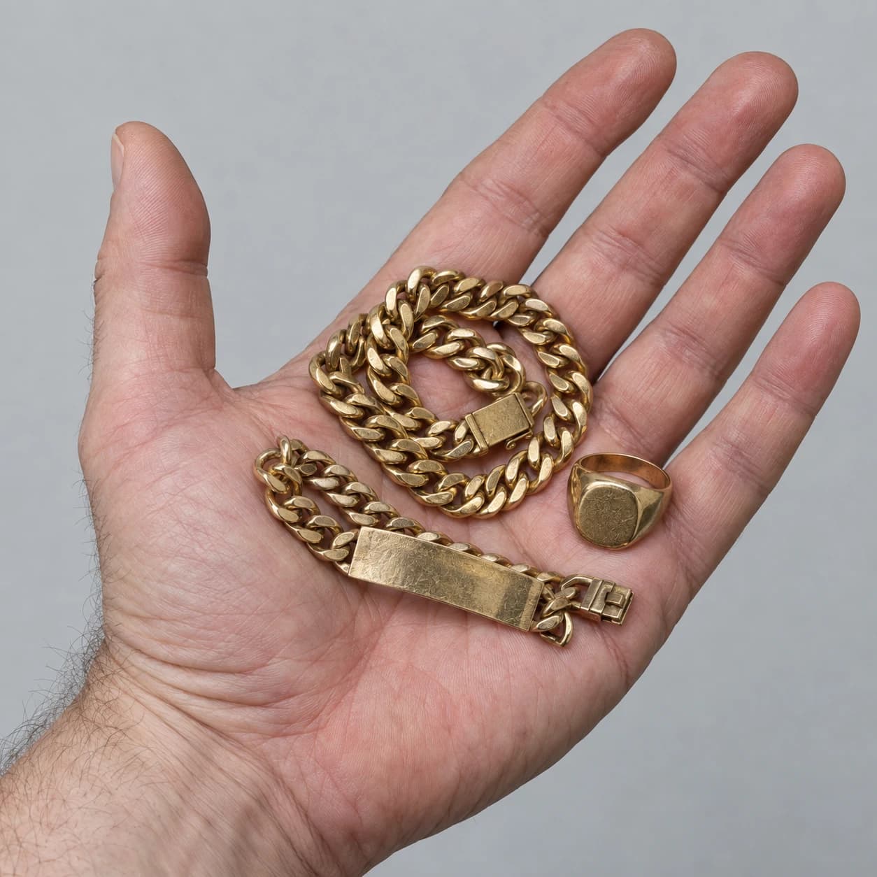 An open hand holding a substantial worn gold chain, bracelet and signet ring
