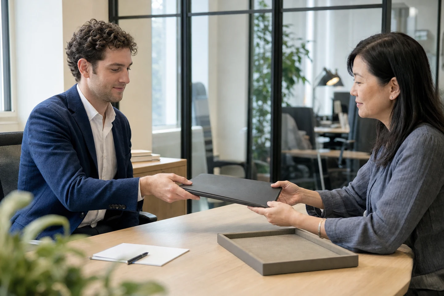 An adviser passing a document folio to a customer across a consultation table