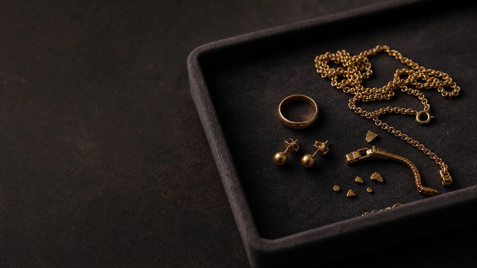 Gold chains, rings and jewellery fragments arranged in a dark valuation tray